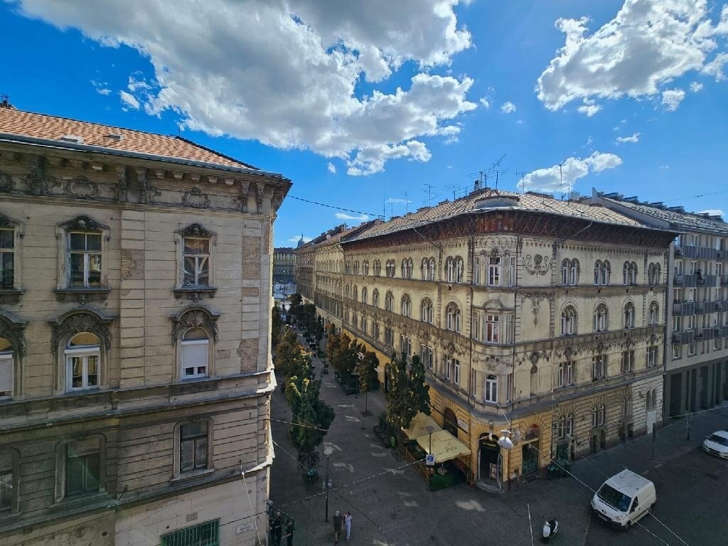 Napos utcakép klasszikus stílusú épületekkel, fákkal és kávézóterasszal - Budapest VII. kerület