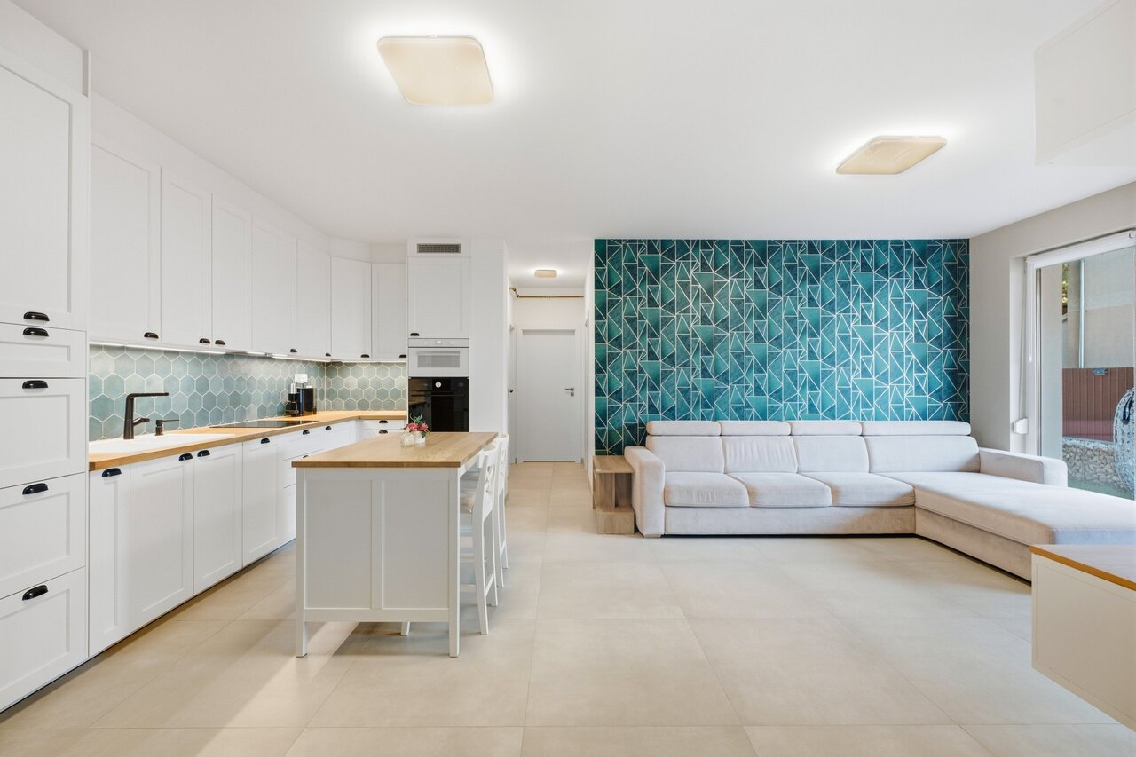 Világos, nyitott terű nappali-konyha sarokkanapéval és petróleumzöld geometrikus tapétával - eladó kertkapcsolatos lakás, Érd