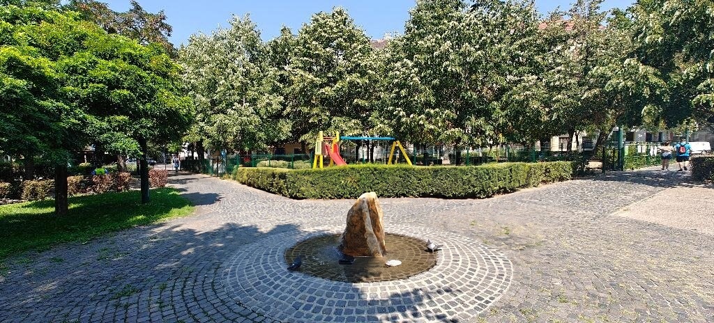Gondozott közpark szökőkúttal, játszótérrel és fákkal a környéken