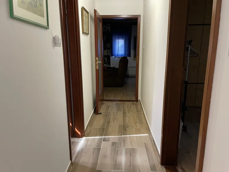 Keskeny közlekedő világos padlóval és kétoldalt nyíló barna ajtókkal.