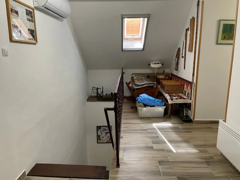 Tetőtéri lépcsőfeljáró fém korláttal, tetőablakkal, fa paddal és fali képekkel.
