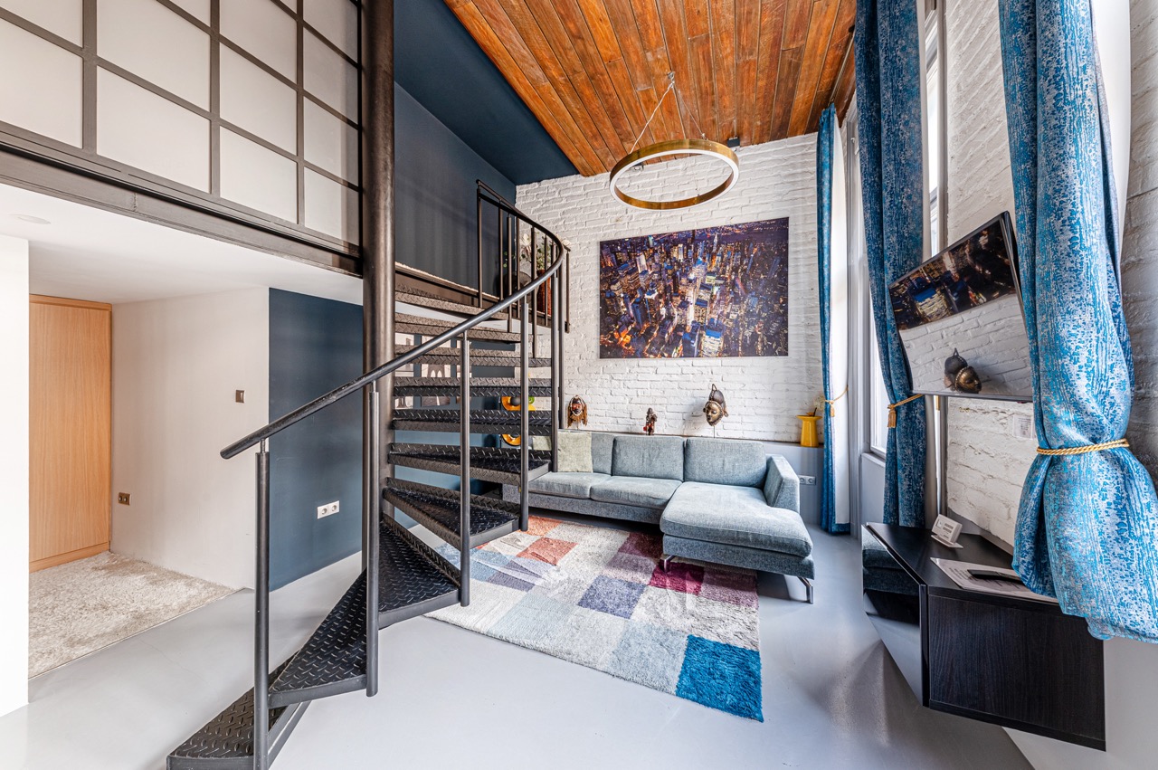 Modern loft nappali fehér téglafalakkal, kék kanapéval és spirál lépcsővel