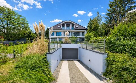 A modern villaépület homlokzata beépített garázzsal, nagy üvegfelületekkel és gondozott kerttel