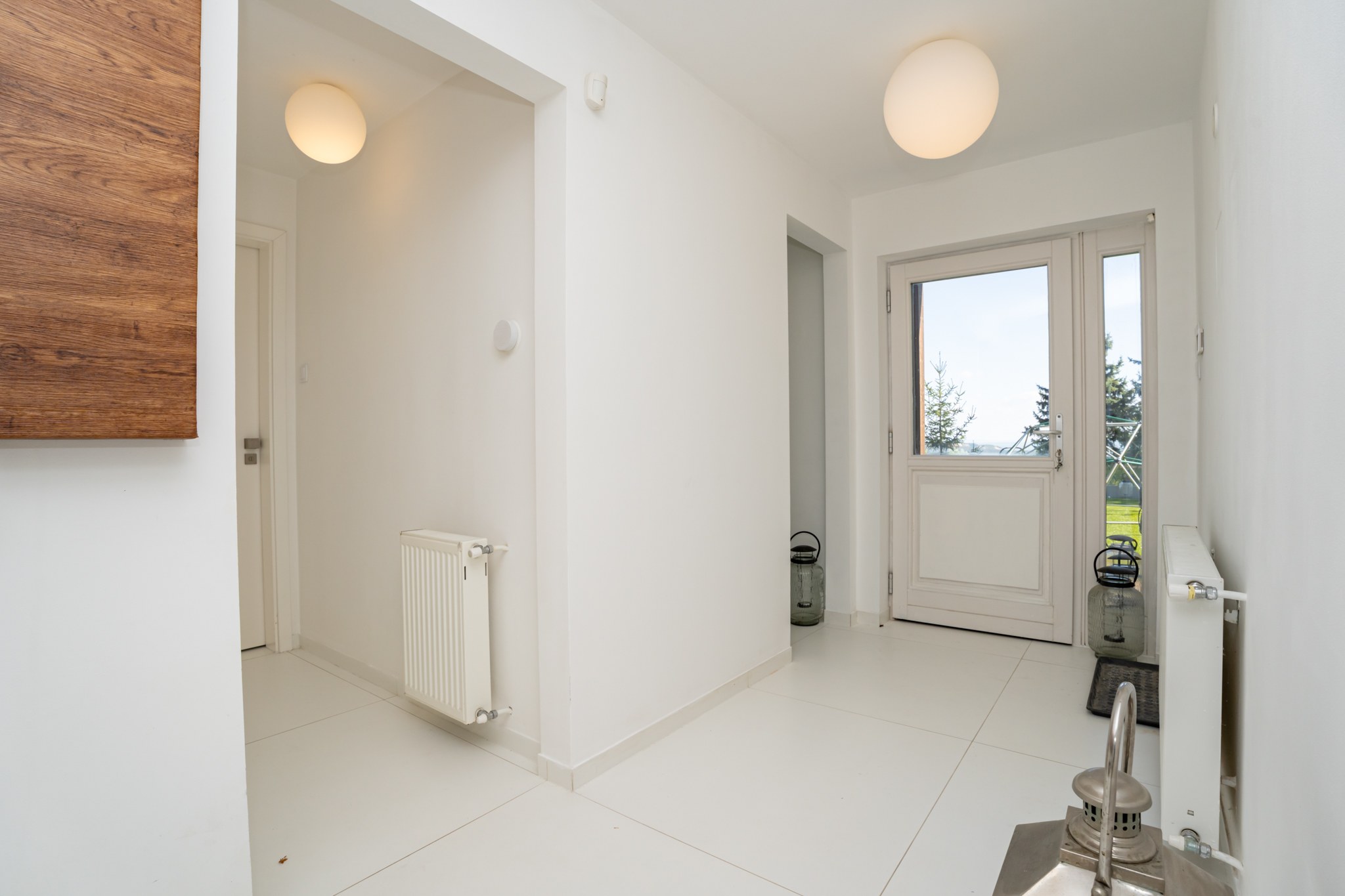 A bright and spacious entrance hall finished in a modern, minimalist style with white walls and flooring. The glazed front door opens directly onto the garden.