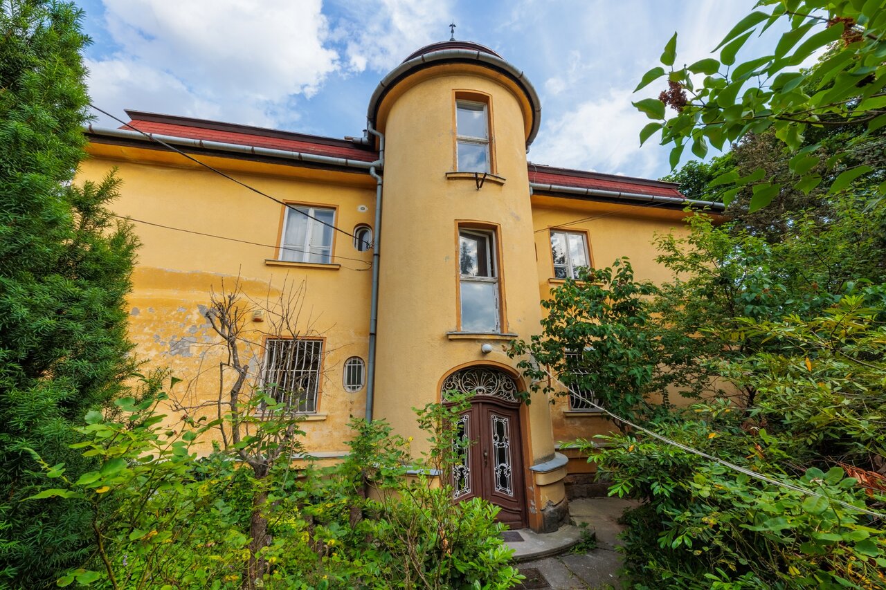 A sárga villaépület kerek toronnyal, dús kertben, felújítás előtt