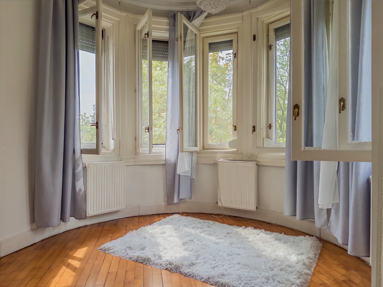 Világos, kerekített falú nappali nagy ablakokkal és meleg tónusú fapadlóval - luxusvilla a Városmajorban, XII. kerület
