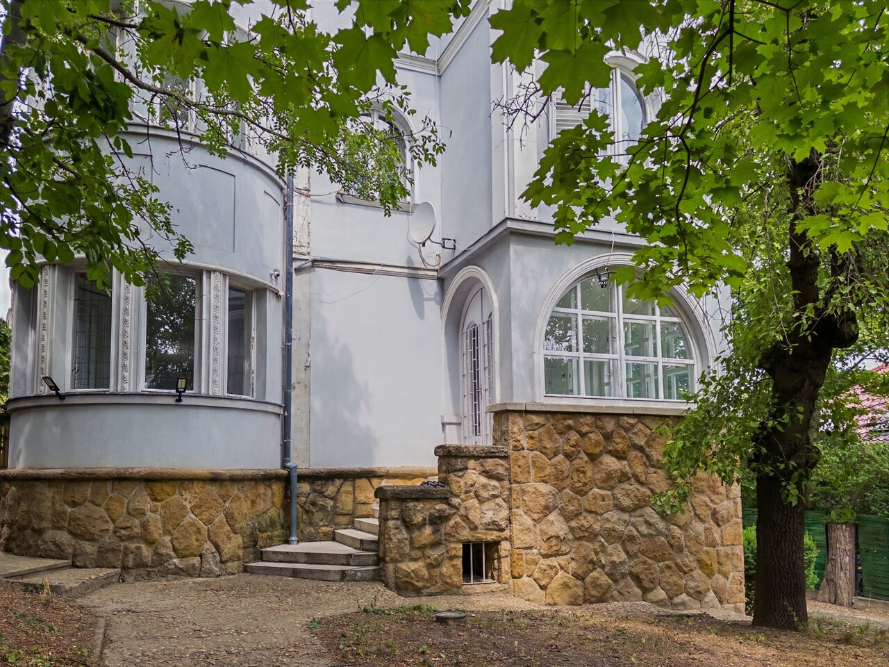 A villa homlokzata terméskő burkolattal, íves és nagyméretű ablakokkal, fák között - eladó luxusvilla, Budapest XII. kerület